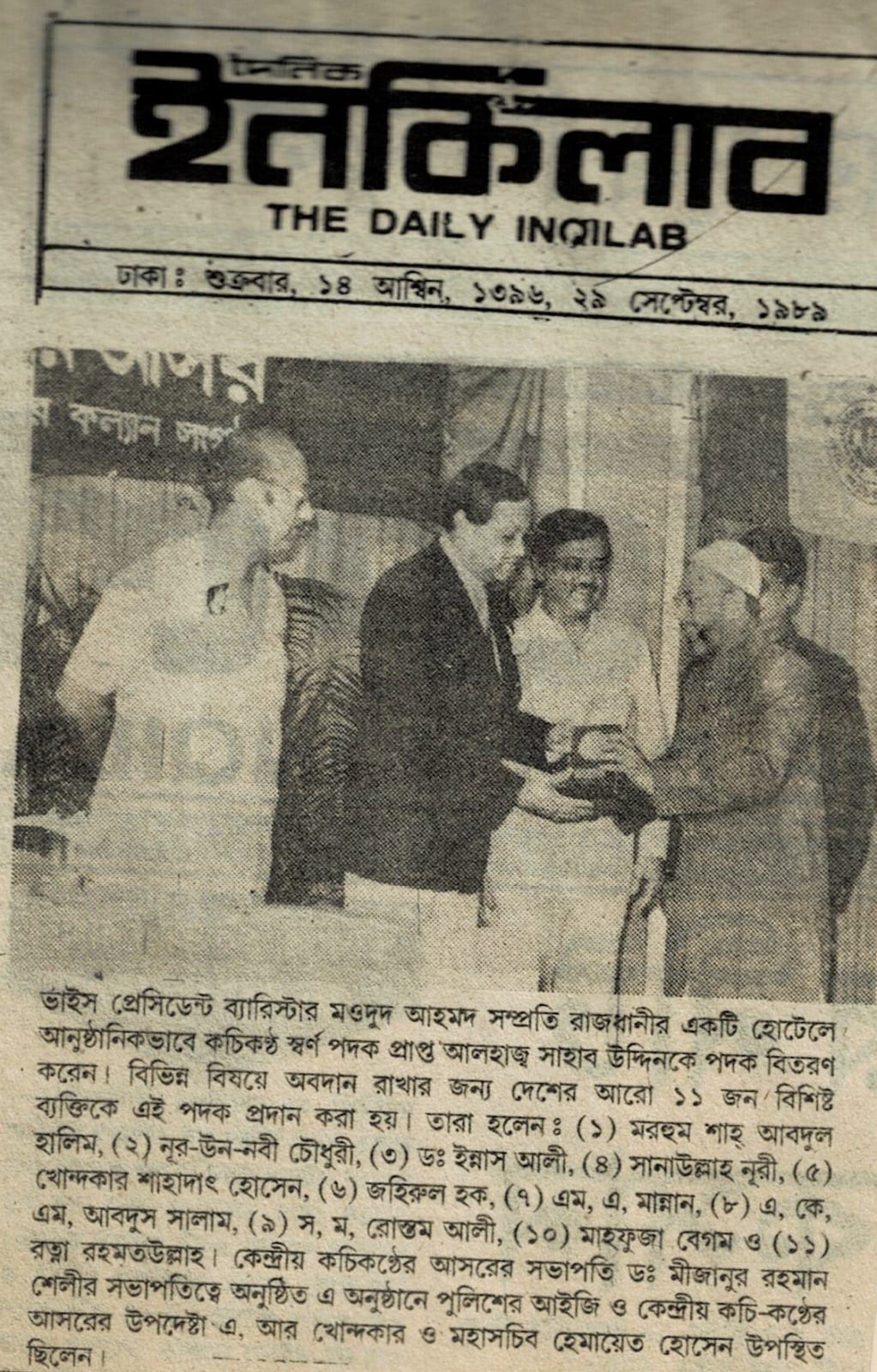 A newspaper page from The Daily Inqilab: a man in a dark suit handing a medal to another man on a stage, with two more men beside them