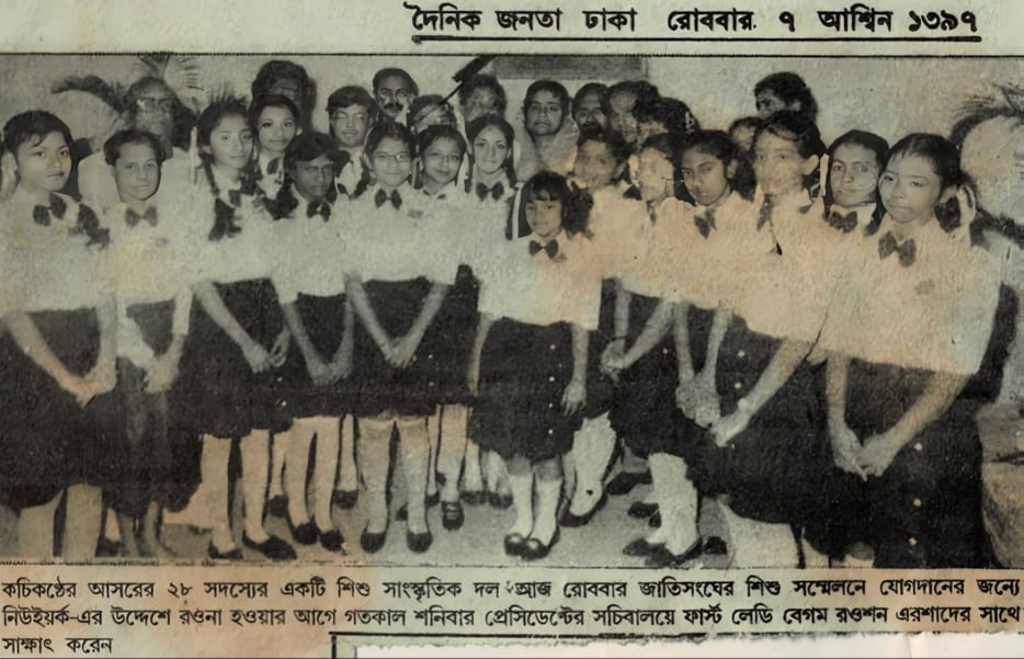 A newspaper photograph: two rows of children in white shirts, dark skirts and bow ties standing shoulder to shoulder