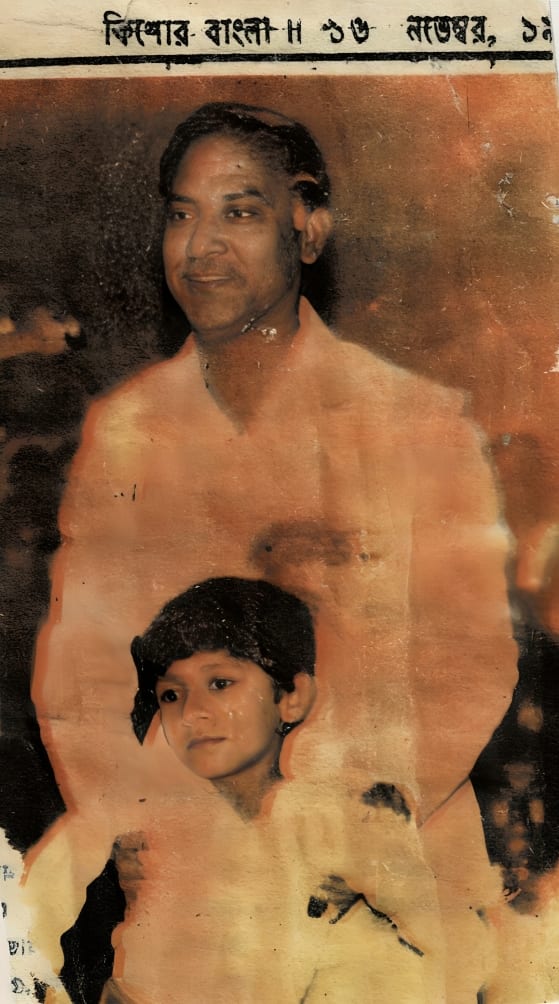 A stained and foxed magazine page: a smiling man in a light jacket standing behind a young child