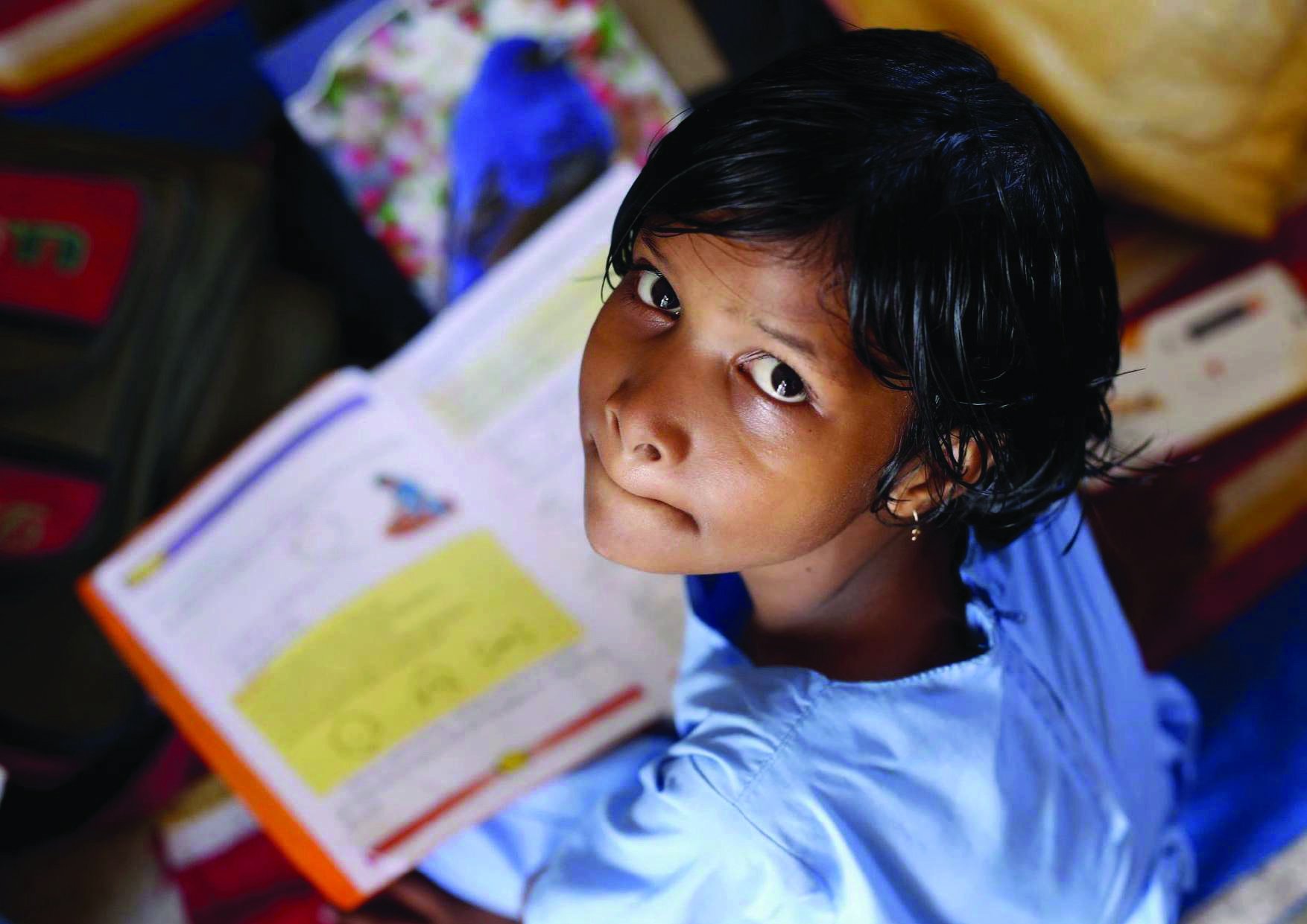 A girl in school uniform sitting on the floor, looking up from an open exercise book