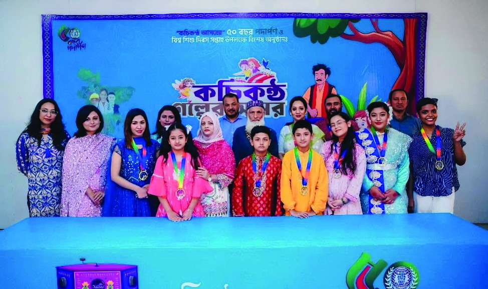 Children wearing medals on a stage, before a backdrop for Kochi Konther Asar’s fiftieth year