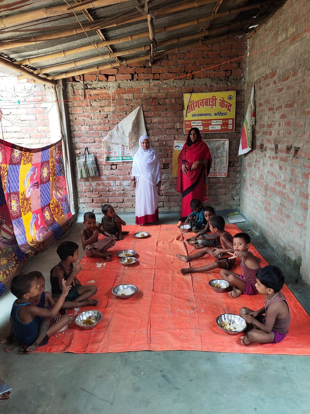 Children sitting on a mat eating a meal from steel plates. Children eating from steel plates on a mat in a community center, India.