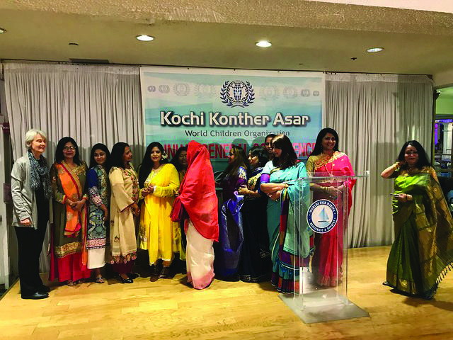 Women in saris standing at a lectern beneath a banner reading “Kochi Konther Asar — World Children Organization”